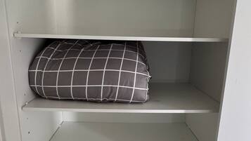 A white closet with three shelves, one of which holds a black and white checkered pillow.