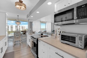 Una cocina moderna con horno empotrado, microondas y tostadora, un comedor con sillas blancas y vistas a la ciudad.