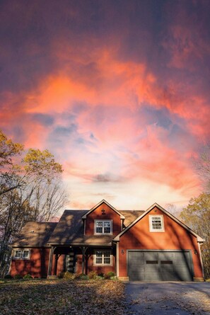 Une maison à deux étages avec un garage, entourée d’arbres et dotée d’une allée.
