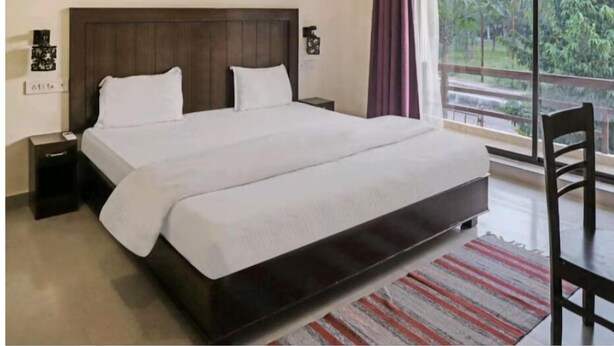 Una cama grande con cabecera de madera, una mesita de noche y vistas a zonas verdes por una ventana.