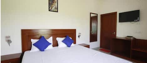 A hotel room with a large bed, a wooden headboard, a flat-screen TV mounted on the wall, and a wooden wardrobe.