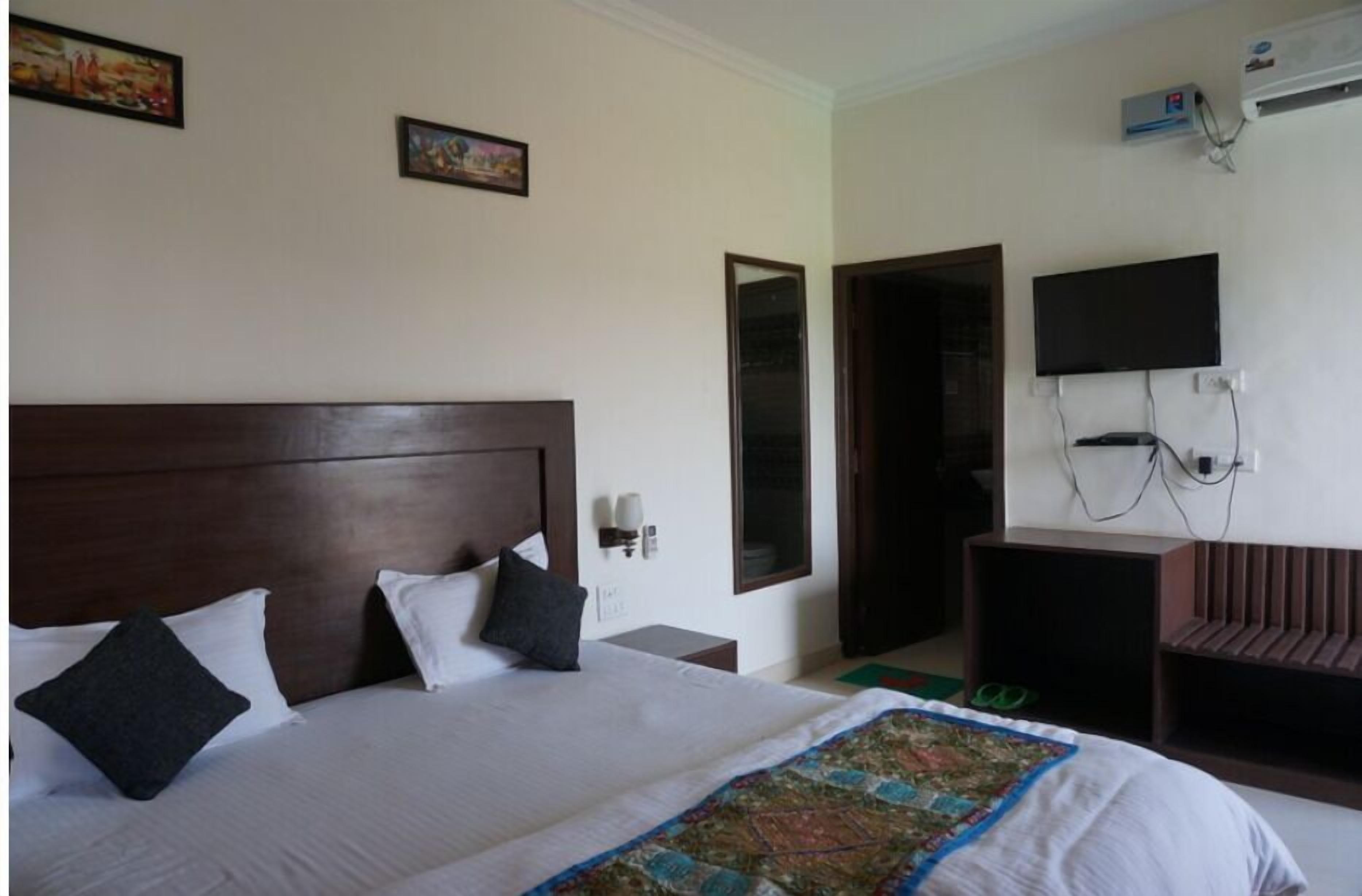 A hotel room with a large bed, a TV, an air conditioning unit, and a door leading to another room.