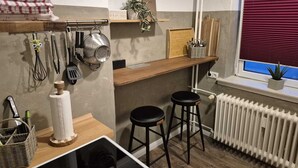 A kitchen with wooden countertops, hanging utensils, a radiator, and a window with blinds.