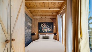 Camera da letto in una baita di legno con un letto, un quadro di fiori e una finestra con tende.