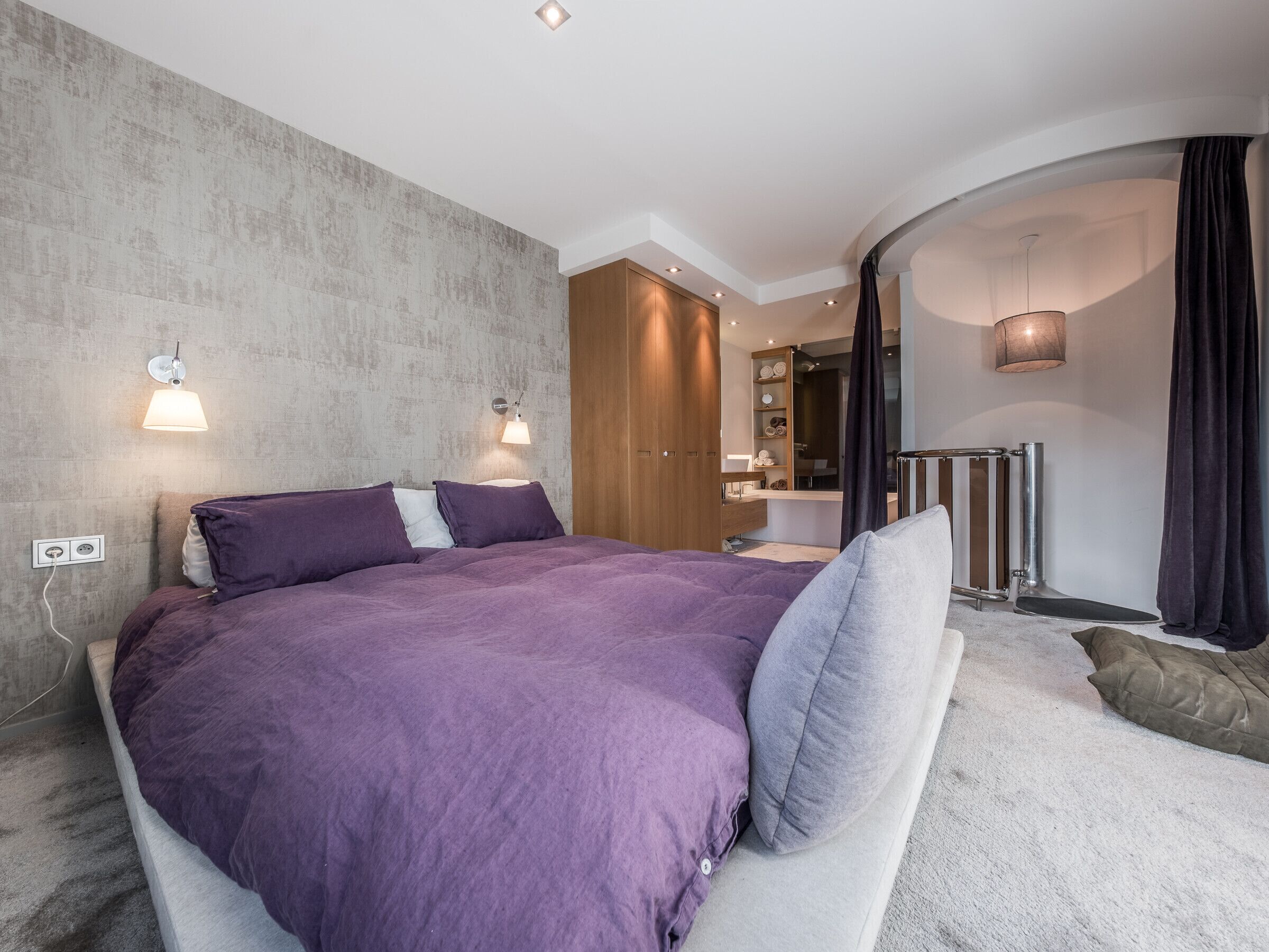 Une chambre moderne avec un grand lit, une armoire, une coiffeuse et une salle de bain.