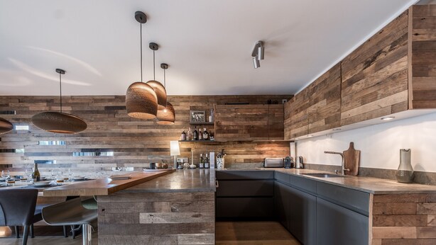 Eine moderne Küche mit einer Wand aus Holzpaneelen, einer zentralen Kochinsel und Pendelleuchten.