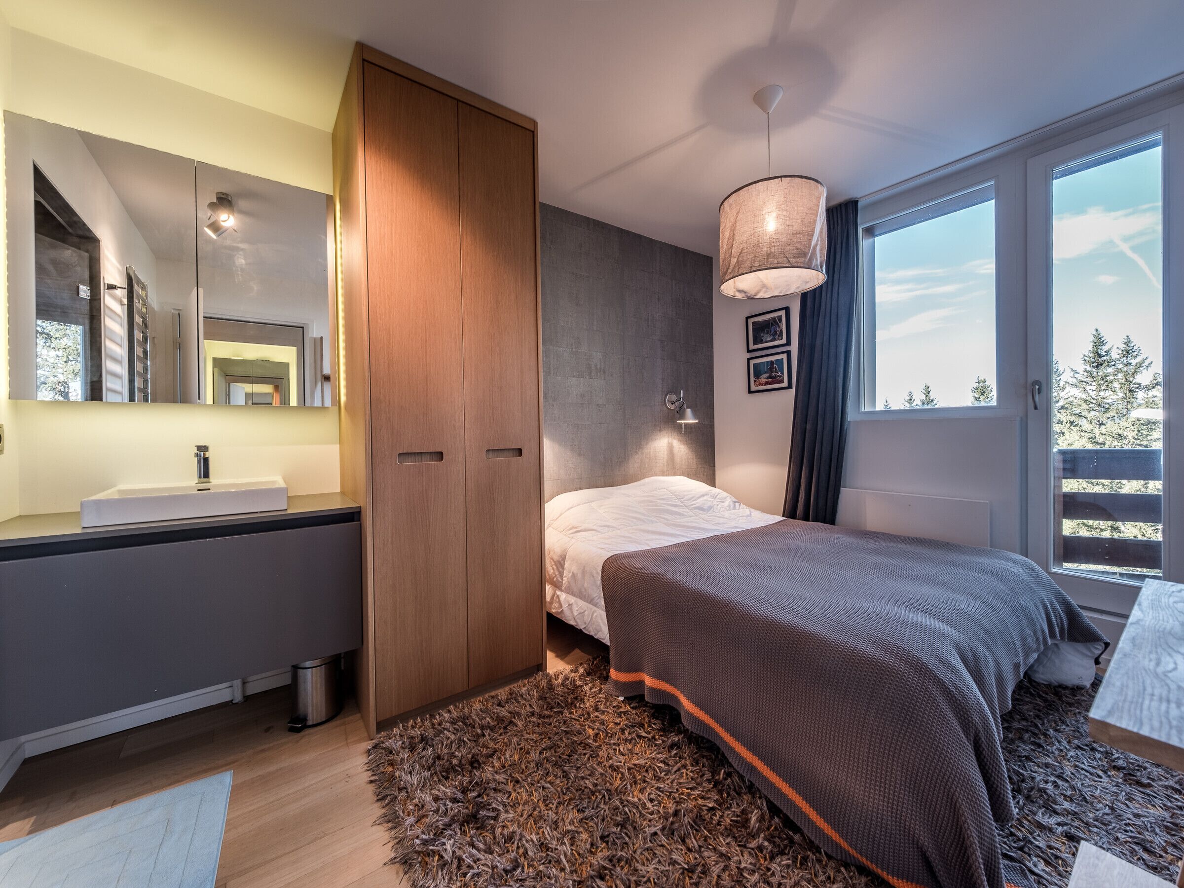 Une chambre moderne dotée d’un grand lit, d’une armoire intégr ée, d’une coiffeuse avec un miroir et d’une grande fenêtre donnant sur la forêt.