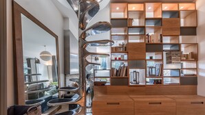 Ein modernes Wohnzimmer mit einer zentralen Metallskulptur, Holzregalen mit Büchern und Dekoration sowie einem gemusterten Teppich.