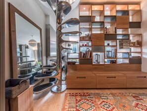 Ein modernes Wohnzimmer mit einer zentralen Metallskulptur, Holzregalen mit Büchern und Dekoration sowie einem gemusterten Teppich.