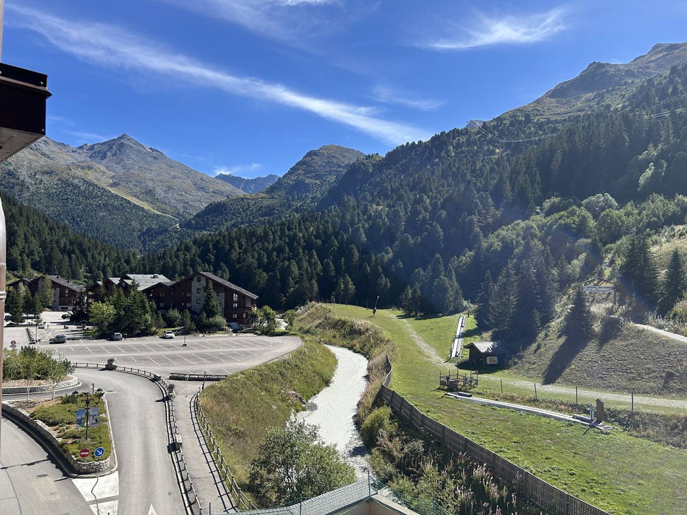 A mountain road with a curve, a parking area, and a building with a view of the surrounding forest and mountains.