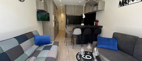 A compact living space with a sofa, a small dining table with glasses, and a kitchen area.