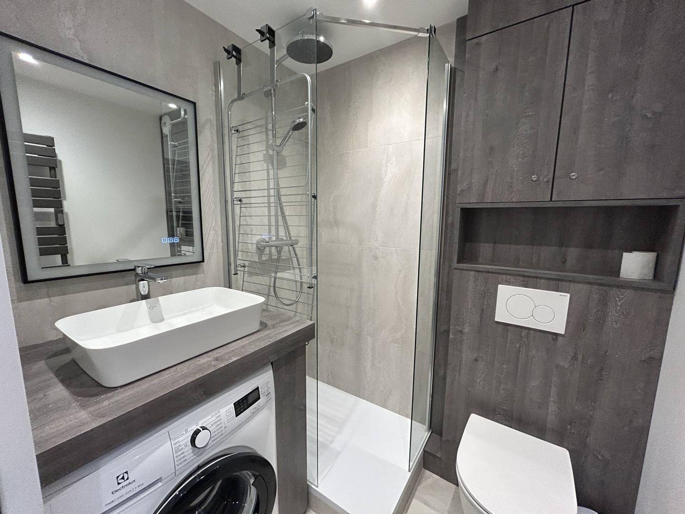A modern bathroom with a built-in washing machine, a glass shower enclosure, and a toilet.