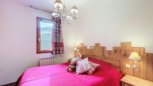 Ein Schlafzimmer mit einem hölzernen Kopfteil, einem großen Fenster mit Vorhängen, einer Chandelieber und Nachttischlampen.