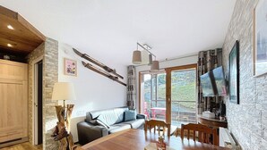 Ein gemütliches Wohnzimmer mit einem Holzesstisch, einer Couch und einem an der Wand montierten Fernseher.