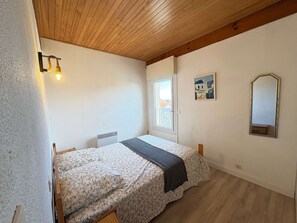 Ein kleines, gemütliches Schlafzimmer mit Holzbalkendecke, einem Bett mit Blumenmuster, einem Nachttisch, einem Fenster mit Aussicht und einem Spiegel an der Wand.