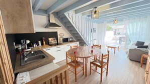 A modern kitchen with white cabinets, a wooden countertop, and a built-in microwave. There is a dining area with a wooden table and chairs, and a staircase leading to an upper level. - Renovated 2023 house close to the ocean with terrace and WIFI (Biscarrosse Plage)