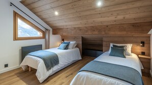 Ein Schlafzimmer mit zwei Betten, Holzboden und einem Fenster mit Blick auf die Berge.