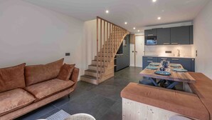 Ein modernes Wohnzimmer mit einem braunen Sofa, einem Esstisch mit blauen Tellern und einer Küche im Hintergrund.