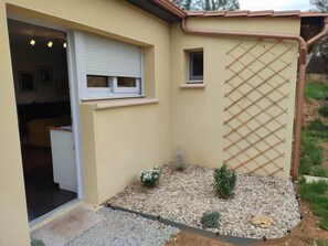 A building with a beige exterior, a white door, a small window, and a lattice screen. - Charming renovated house in Sarlat with air conditioning and private parking (Sarlat-la-Canéda)