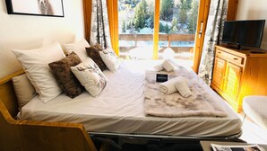 A bed with a white mattress, multiple pillows, a blanket, and a towel. There is a television on a wooden cabinet, and a framed picture of a deer on the wall. - Ski-in duplex for 4 with parking in Méribel (Méribel)
