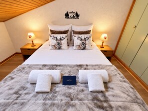 Ein ordentlich bezogenes Bett mit zwei Kissen mit Hirschmuster, zwei Nachttischlampen, einem flauschigen Teppich und einer kleinen Karte auf dem Bett.