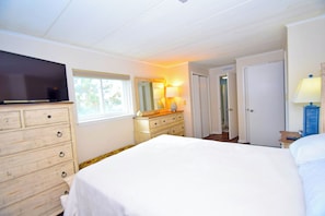 Een slaapkamer met een bed, een dressoir, een televisie en een lamp.
