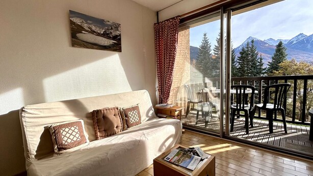 A cozy room with a sofa, a small table, and a large window offering a mountain view. - Studio with balcony and parking - Briançon 4 people (Briançon)
