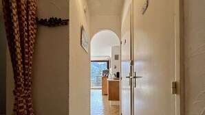 A narrow hallway with a checkered curtain on the left, leading to a room with a tiled floor and a view of a balcony. - Studio with balcony and parking - Briançon 4 people (Briançon)