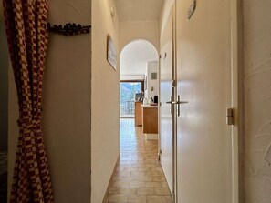 A narrow hallway with a checkered curtain on the left, leading to a room with a tiled floor and a view of a balcony. - Studio with balcony and parking - Briançon 4 people (Briançon)