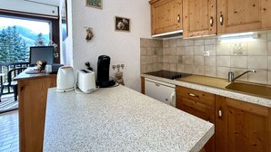 A kitchen with wooden cabinets, a countertop, a stove, and a sink. There is a window with a view of trees and mountains. - Studio with balcony and parking - Briançon 4 people (Briançon)