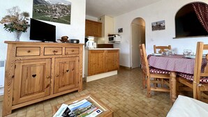 A cozy living room with a wooden cabinet, a television, and a dining table with chairs. - Studio with balcony and parking - Briançon 4 people (Briançon)