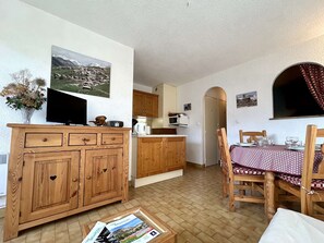 A cozy living room with a wooden cabinet, a television, and a dining table with chairs. - Studio with balcony and parking - Briançon 4 people (Briançon)