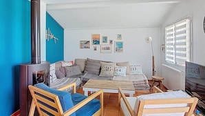 A cozy living room with a sofa, wooden chairs, a coffee table, and a TV. There is a blue wall and a window with blinds. - Villa in Vieux-Boucau for 10, near ocean, with terrace (Vieux-Boucau-les-Bains)