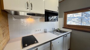Een compacte keuken met witte kasten, een inbouwmagnetron, een kookplaat en een raam met uitzicht op besneeuwde bomen.