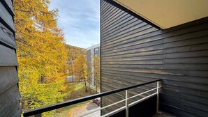 Een balkon met een metalen hekwerk, met uitzicht op een bos in herfstkleuren.