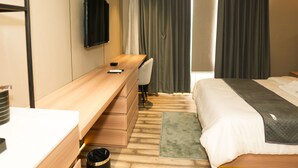 Ett hotellrum med en säng, ett skrivbord, en stol, en tv och en papperskorg.