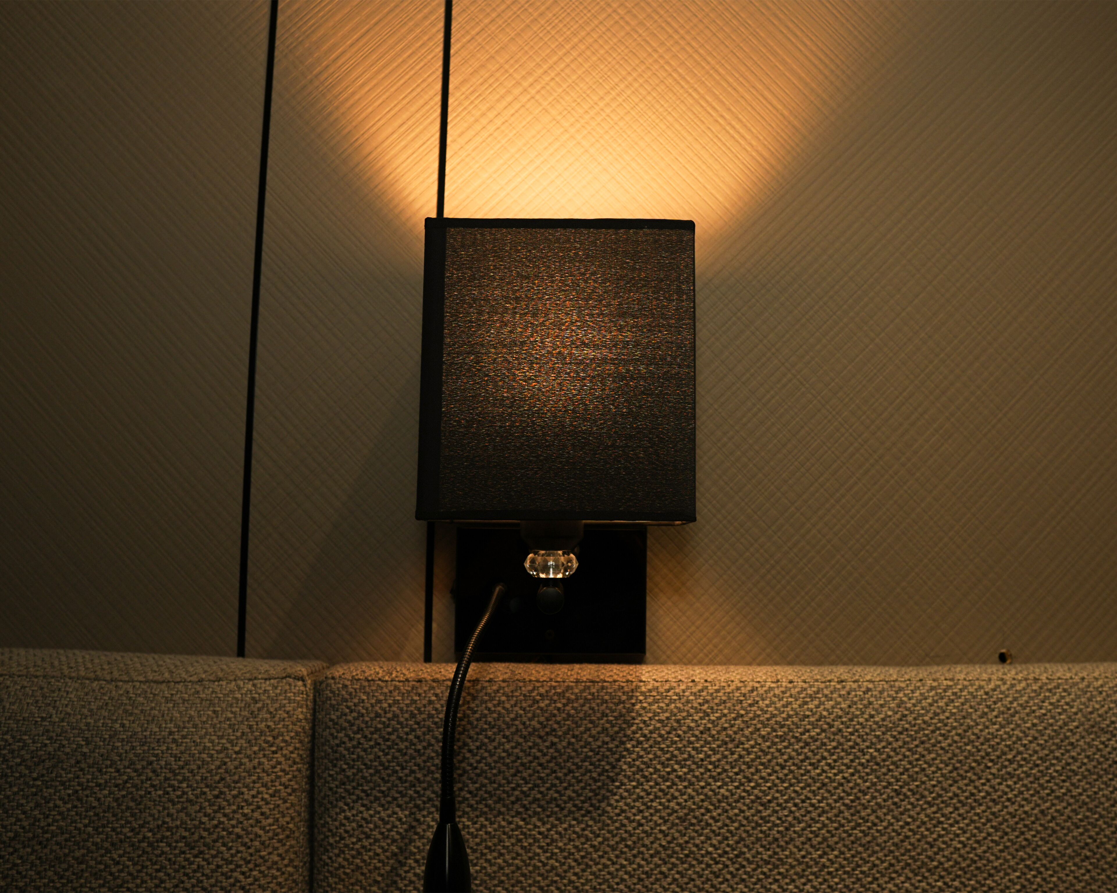 A wall-mounted lamp with a textured shade, a visible power cord, and a textured wall behind it.