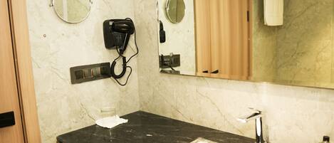 A bathroom with a marble wall, a black sink, a mirror, a hairdryer, and a towel rack.