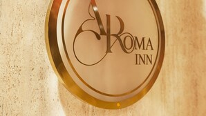 En rund skylt med texten ”ROMA INN” och en stiliserad logotyp i form av bokstaven ”R”.