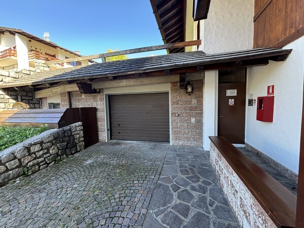 A building with a stone facade, a closed garage door, and a red fire safety box. - Casa D’Ajal – Cortina Between Nature and Mountain View (Cortina d´Ampezzo)