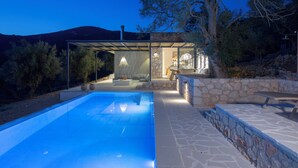Un área de piscina moderna al aire libre con paredes de piedra, un espacio para sentarse y vistas del paisaje circundante.