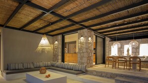 Un interior moderno con una pared de piedra, una zona de estar con cojines, una mesa de comedor con sillas y una lámpara colgante.