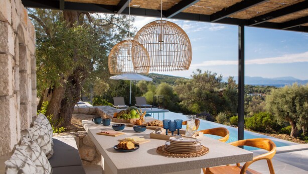 Un espacio exterior para comer con una mesa de piedra, sillas y vistas a una piscina y al paisaje.