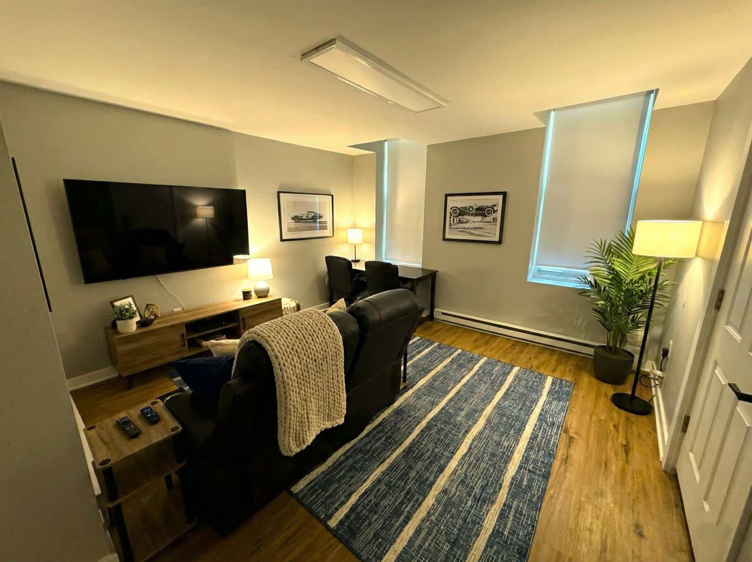 Un salon moderne avec un téléviseur à écran plat, un canapé, une table basse, une lampe et des tableaux encadrés accrochés au mur.