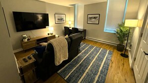 Un salon moderne avec un téléviseur à écran plat, un canapé, une table basse, une lampe et des tableaux encadrés accrochés au mur.