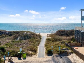 A beach pathway leading to the ocean with a wooden fence on one side and a building on the other. - 4bdrm OKI Gem - Steps to Beach with Poolside Oasis (Oak Island)