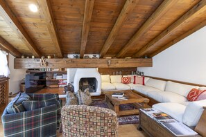 Un salon chaleureux avec une cheminée, des poutres apparentes en bois au plafond, un ensemble de canapés et une table basse.