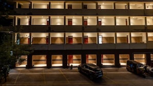 Un hotel de varios pisos con balcones iluminados y un estacionamiento.