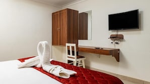Una habitación de hotel con una cama, un armario de madera, un escritorio con silla, un televisor y una manta roja.