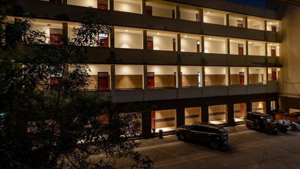 Un hotel de varios pisos con habitaciones individuales en cada planta, un estacionamiento y una pequeña área ajardinada.